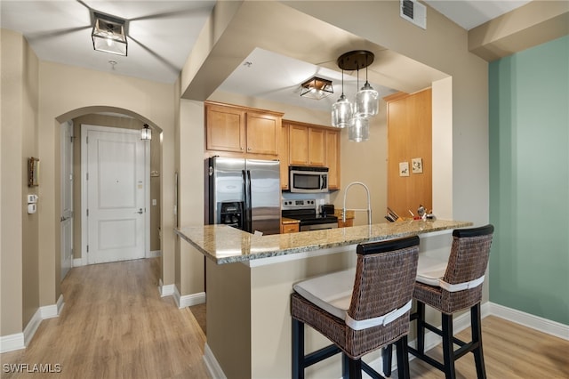 kitchen with kitchen peninsula, appliances with stainless steel finishes, light hardwood / wood-style flooring, and light stone countertops