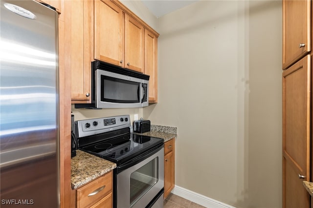 kitchen featuring baseboards, appliances with stainless steel finishes, light tile patterned floors, and light stone countertops