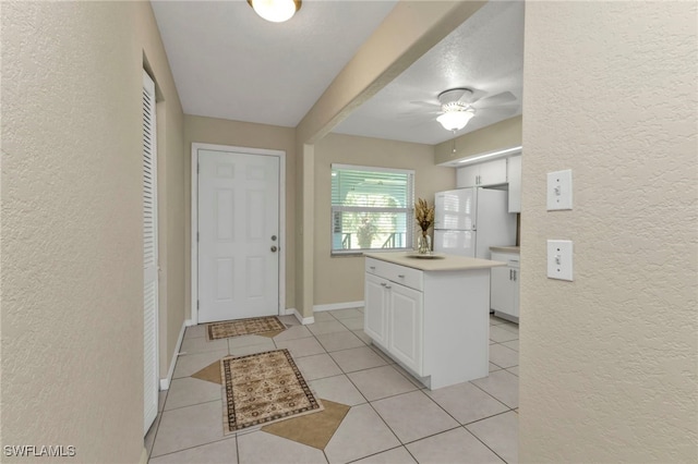 kitchen featuring a textured ceiling, white cabinets, a kitchen island, white refrigerator, and light tile patterned floors