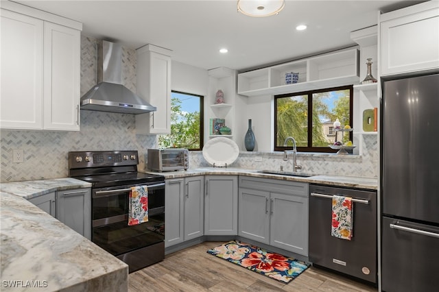 kitchen featuring white cabinetry, sink, wall chimney exhaust hood, light hardwood / wood-style floors, and appliances with stainless steel finishes