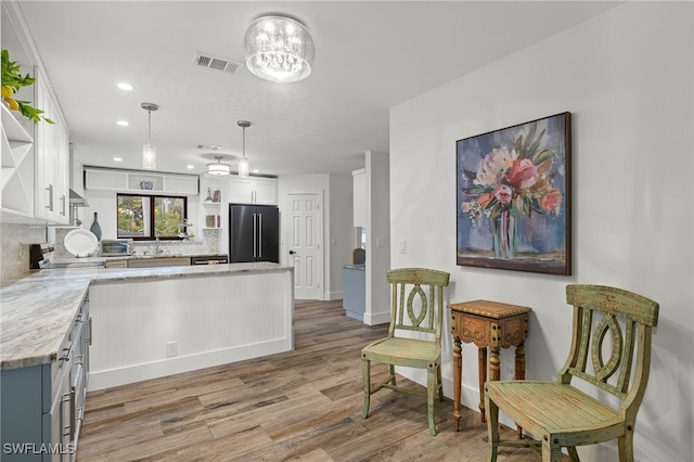 kitchen with backsplash, high end refrigerator, light stone countertops, light wood-type flooring, and white cabinetry