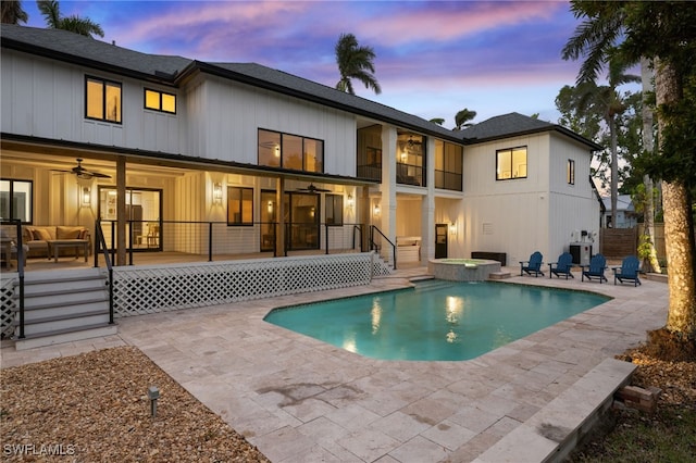 back house at dusk with ceiling fan, a swimming pool with hot tub, and a patio