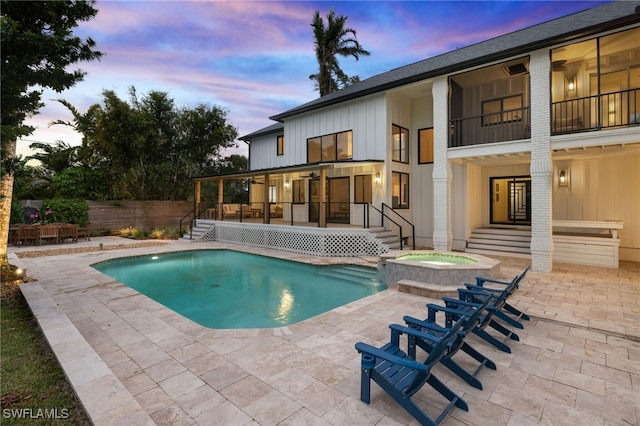 pool at dusk with a patio area and an in ground hot tub