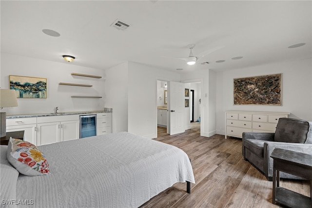 bedroom featuring ceiling fan, light hardwood / wood-style flooring, ensuite bathroom, and beverage cooler