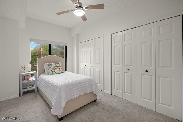 bedroom featuring multiple closets, light carpet, ceiling fan, and a textured ceiling