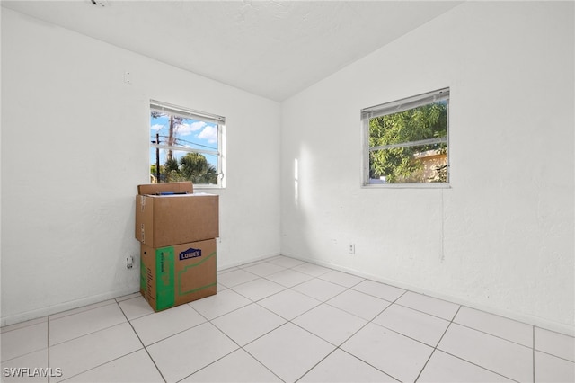 spare room featuring light tile patterned floors, a healthy amount of sunlight, and lofted ceiling