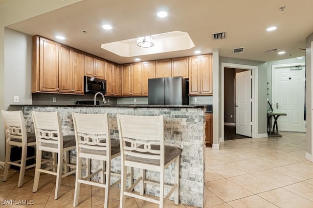 kitchen with a breakfast bar, dark stone counters, appliances with stainless steel finishes, light tile patterned flooring, and kitchen peninsula