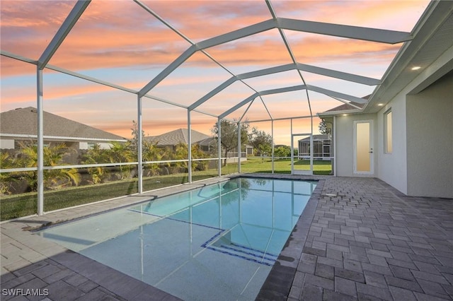 pool at dusk with glass enclosure and a patio area