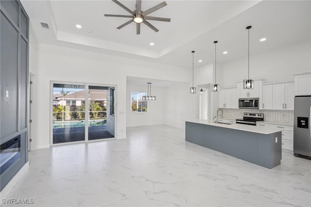 kitchen with white cabinets, a raised ceiling, a kitchen island with sink, and appliances with stainless steel finishes