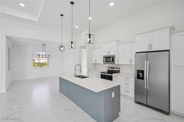 kitchen featuring stainless steel appliances, sink, white cabinets, hanging light fixtures, and an island with sink