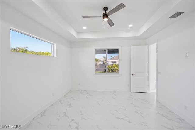 empty room featuring a raised ceiling, ceiling fan, and plenty of natural light