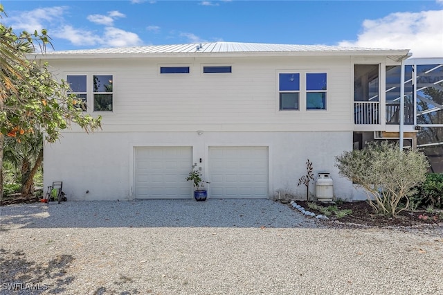 view of side of property featuring a garage, metal roof, gravel driveway, and stucco siding