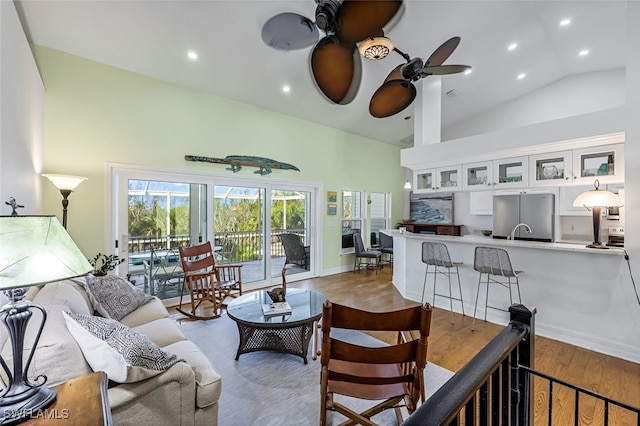 living area with recessed lighting, a ceiling fan, high vaulted ceiling, light wood-type flooring, and baseboards