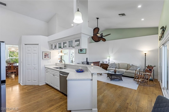 kitchen with glass insert cabinets, a peninsula, stainless steel appliances, white cabinetry, and a sink