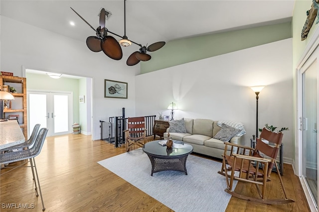 living room featuring french doors, light wood finished floors, lofted ceiling, ceiling fan, and baseboards