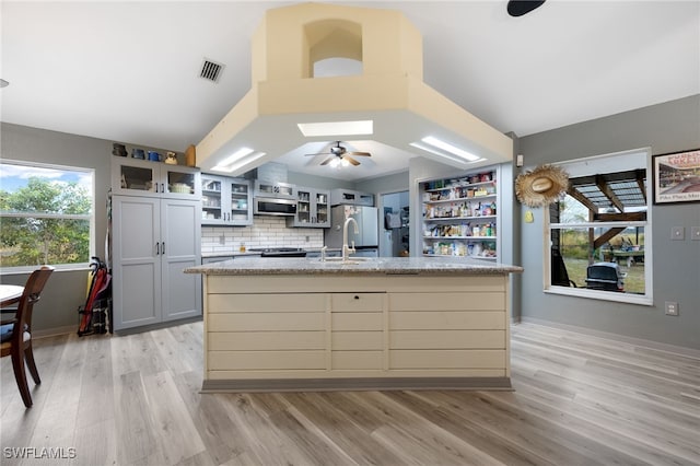 2915 Ortona Locks Rd, Moore Haven, FL 33471 - kitchen with stainless steel microwave, light wood-type flooring, vaulted ceiling, ceiling fan, and a center island with sink