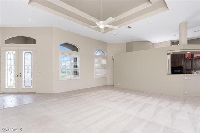 unfurnished living room with ceiling fan, french doors, a raised ceiling, and light carpet