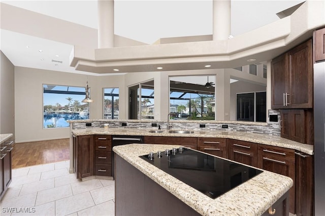 kitchen with black electric stovetop, a water view, light stone countertops, sink, and light tile patterned flooring