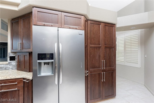 kitchen with light stone countertops, light tile patterned floors, stainless steel refrigerator with ice dispenser, and decorative backsplash