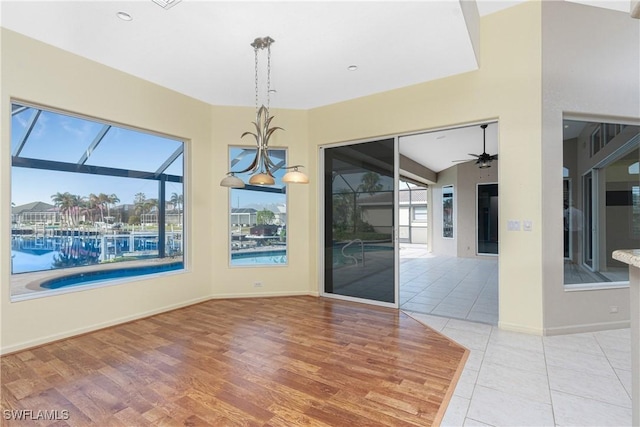 unfurnished dining area featuring lofted ceiling, a wealth of natural light, ceiling fan with notable chandelier, and light tile patterned floors