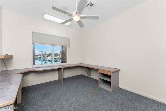 unfurnished office with built in desk, dark colored carpet, and ceiling fan