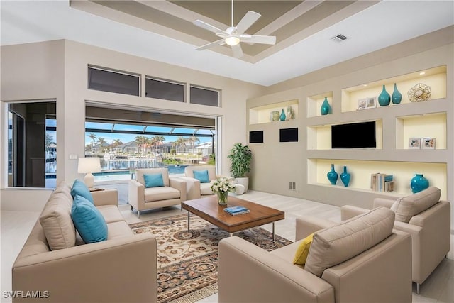 living room featuring ceiling fan, built in features, and a raised ceiling