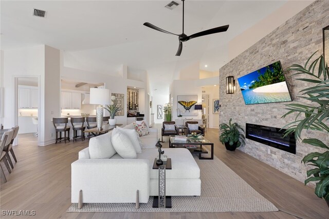 living room with ceiling fan, light wood-type flooring, a fireplace, and high vaulted ceiling