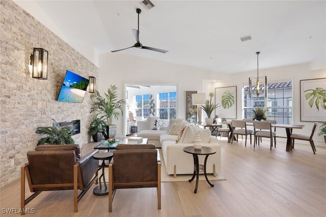 living room featuring a fireplace, ceiling fan with notable chandelier, light hardwood / wood-style flooring, and vaulted ceiling