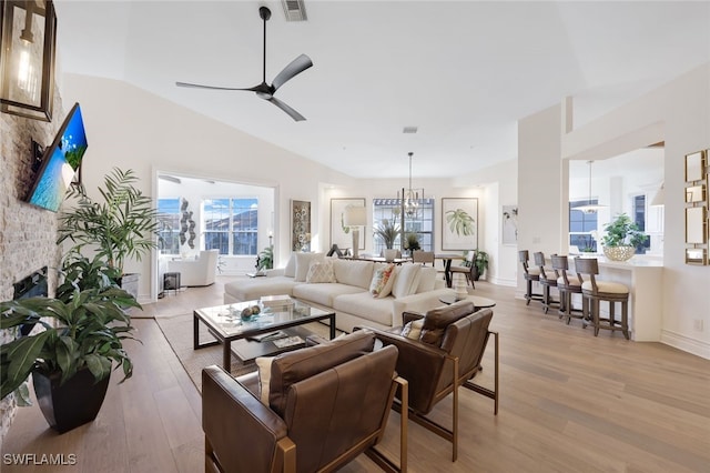 living room with light wood-type flooring, vaulted ceiling, ceiling fan, and a stone fireplace