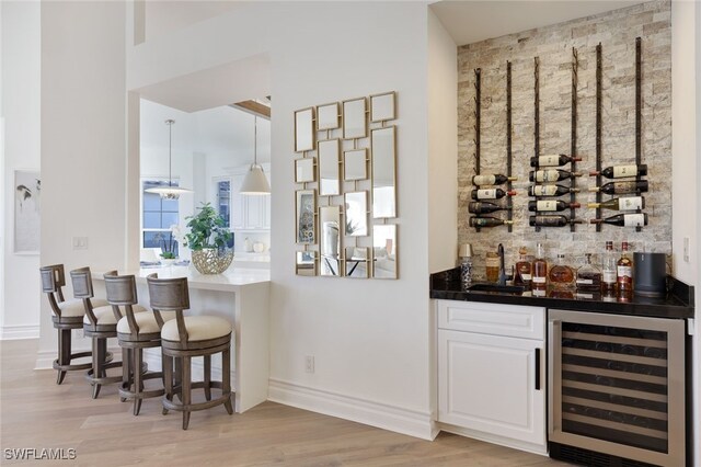 bar featuring white cabinets, sink, light wood-type flooring, decorative light fixtures, and beverage cooler