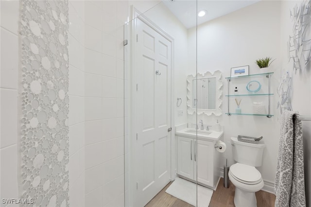 bathroom featuring wood-type flooring, vanity, a tile shower, and toilet