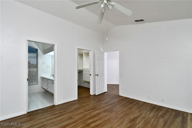 unfurnished bedroom with lofted ceiling, dark wood-type flooring, ensuite bathroom, a walk in closet, and ceiling fan