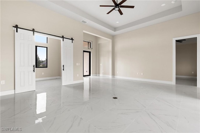 unfurnished room with ceiling fan, a barn door, and a tray ceiling