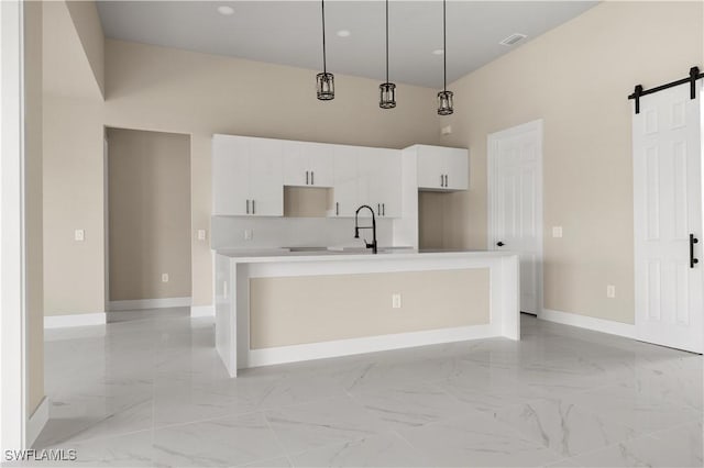 kitchen with a kitchen island with sink, sink, a barn door, white cabinetry, and hanging light fixtures