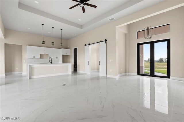 unfurnished living room with a barn door, a raised ceiling, ceiling fan, and sink