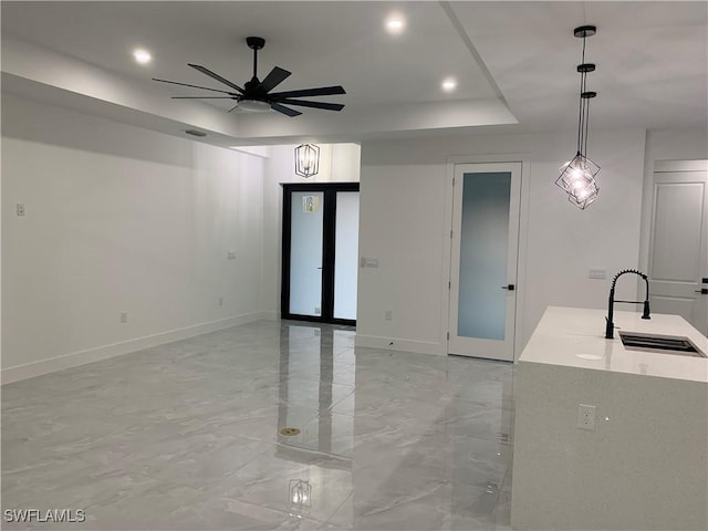 interior space with light stone counters, a tray ceiling, ceiling fan, sink, and pendant lighting