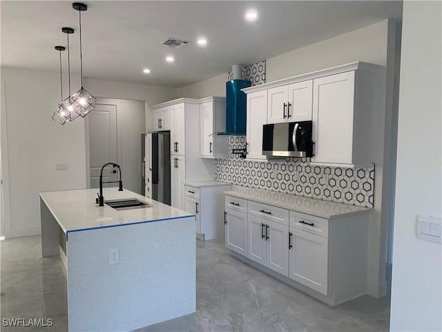 kitchen with white cabinetry, sink, stainless steel appliances, pendant lighting, and a kitchen island with sink