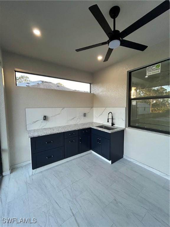 kitchen with ceiling fan, light stone countertops, and sink