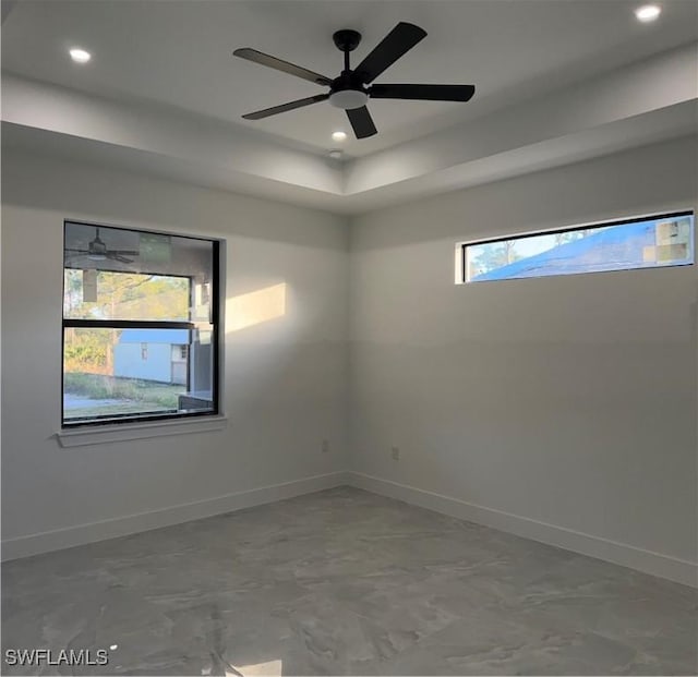 empty room with ceiling fan, a healthy amount of sunlight, and a raised ceiling