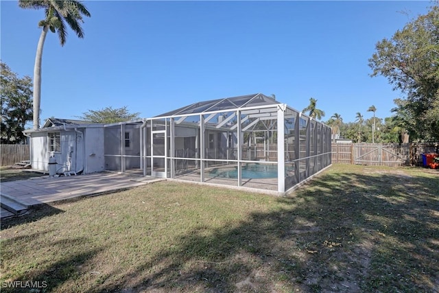 rear view of property featuring a lawn, glass enclosure, a patio area, and a fenced in pool