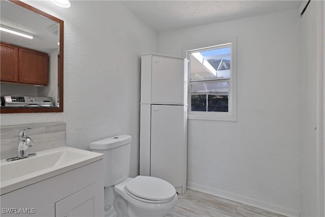 bathroom with washer / clothes dryer, wood-type flooring, a textured ceiling, toilet, and vanity