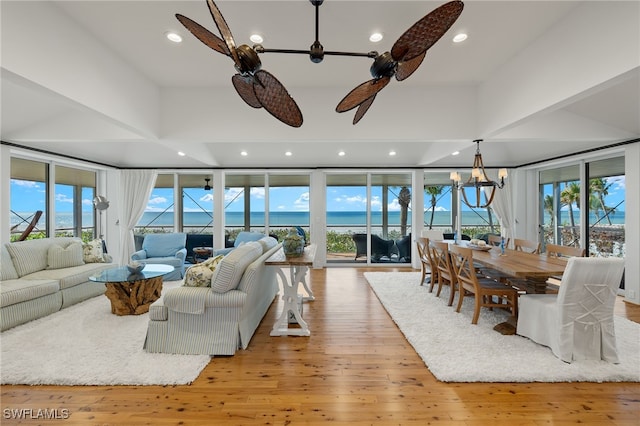 living room featuring light wood-type flooring, ceiling fan with notable chandelier, a water view, and plenty of natural light