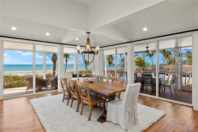 dining room with a water view, a view of the beach, light wood-type flooring, a healthy amount of sunlight, and a chandelier