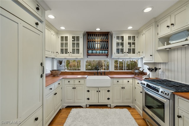 kitchen featuring butcher block counters, high end stainless steel range, white cabinets, and sink