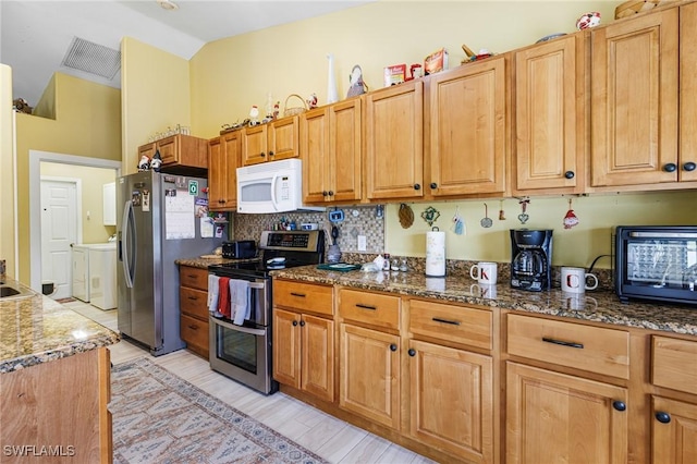 kitchen with lofted ceiling, appliances with stainless steel finishes, independent washer and dryer, dark stone counters, and decorative backsplash