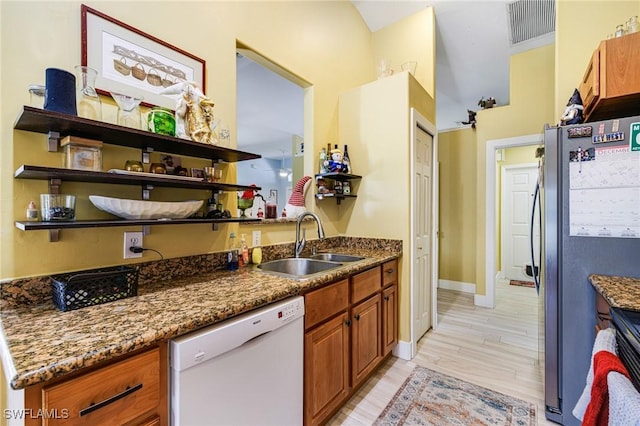 kitchen featuring sink, light wood-type flooring, stainless steel refrigerator, dishwasher, and dark stone counters