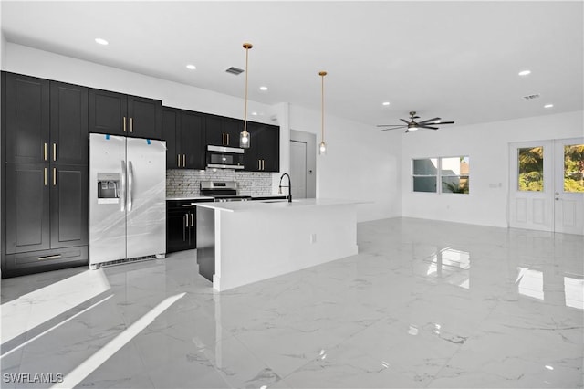 kitchen featuring appliances with stainless steel finishes, backsplash, ceiling fan, a kitchen island with sink, and hanging light fixtures