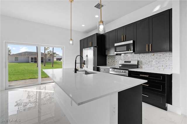 kitchen with decorative backsplash, appliances with stainless steel finishes, sink, hanging light fixtures, and an island with sink