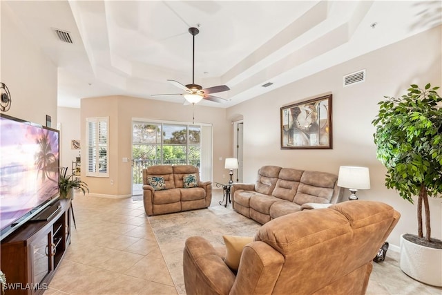 living room featuring light tile patterned floors, ceiling fan, and a tray ceiling