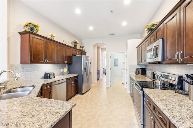 kitchen with sink, backsplash, stainless steel appliances, light stone counters, and washer / dryer